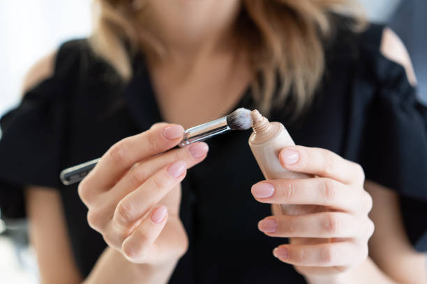 Woman applying liquid foundation to a brush, illustrating makeup application techniques.